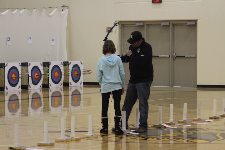 A middle school girl receives help with her bow before taking a shot. 