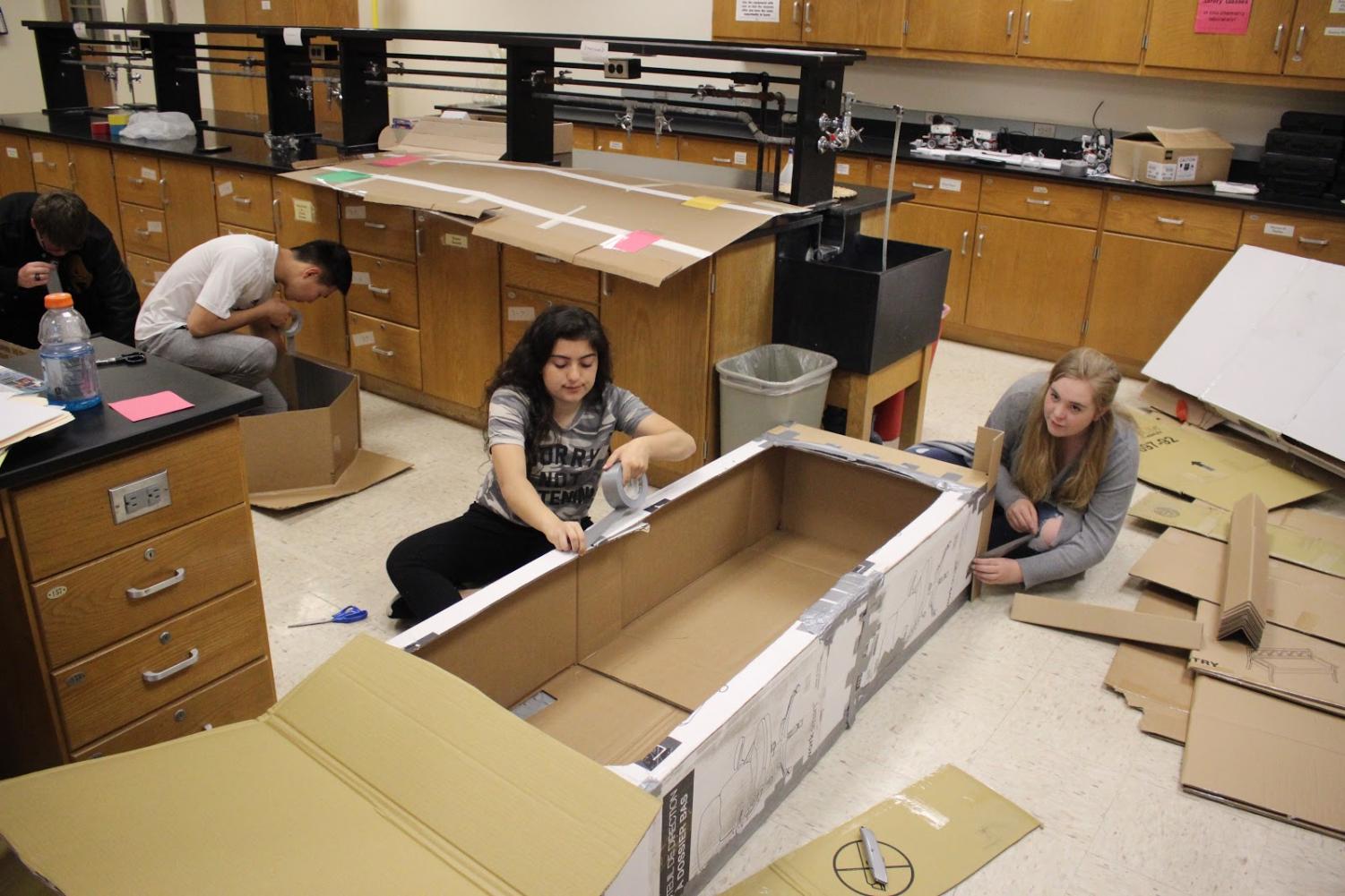 Junior Yara Haidar and senior Paige Bennett work to build their boat. They were given three days in class to work on these and whatever doesn't get finished will have to be done on their own time.