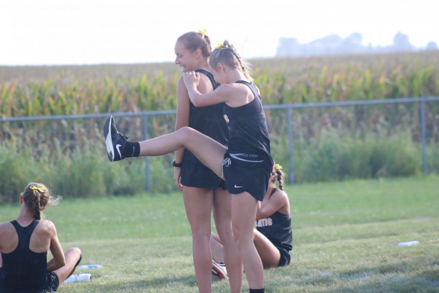 GETTING FOCUSED- Freshman Addie DeArment uses junior Pluma Pross to help her stretch before the race. Other members of the varsity team were stretching before the race at Dallas-Center Grimes. 