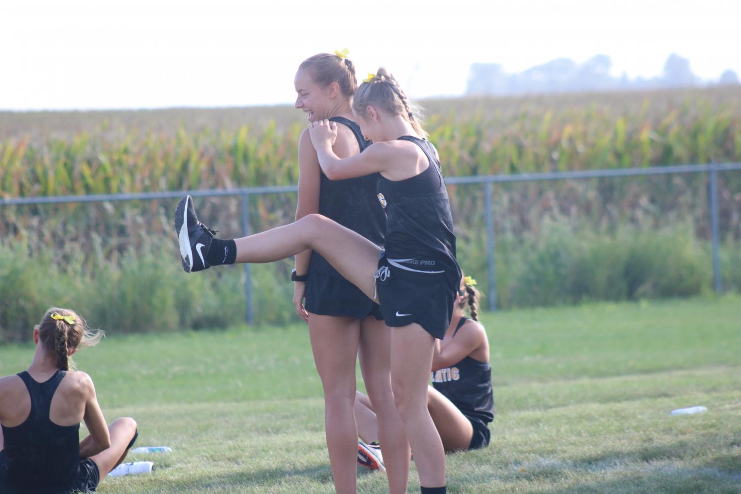 GETTING FOCUSED- Freshman Addie DeArment uses junior Pluma Pross to help her stretch before the race. Other members of the varsity team were stretching before the race at Dallas-Center Grimes.