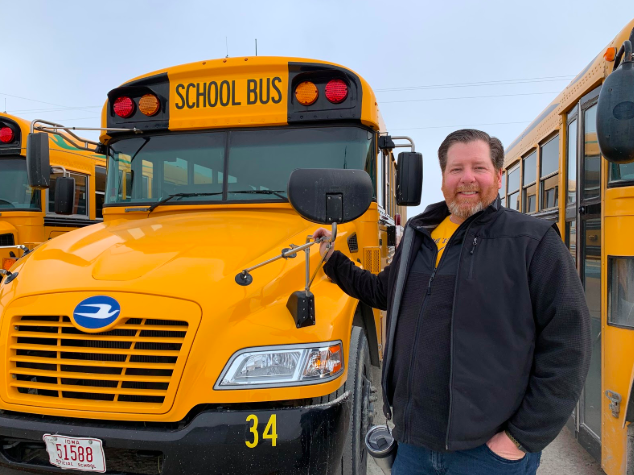 Atlantic Community School District bus driver Steve Andersen stands by one of the many buses at the bus barn on the edge of town. Andersen is one of the eight regular route bus drivers.