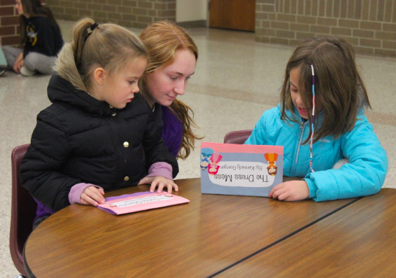 Junior Kennedy Goergen shows two elementary students the book she wrote for her English 3 class. Goergen volunteers at Washington Elementary everyday.