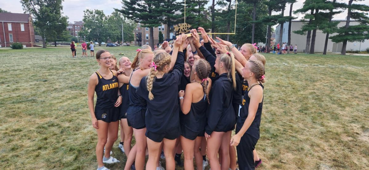 The girls cross country team hoists a trophy above them as they celebrate. The team won the 2023 Clarinda Invitational.
