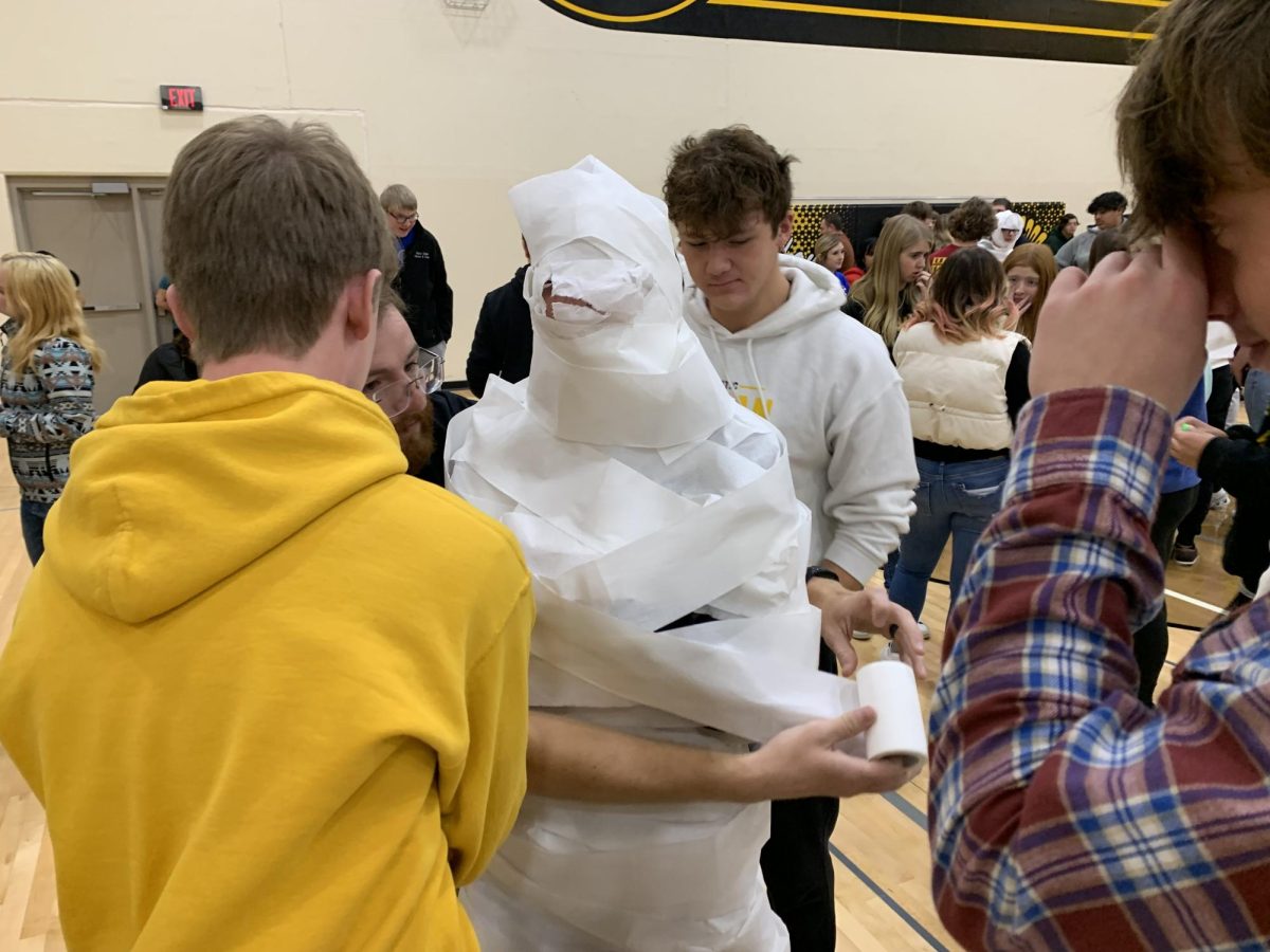 Students work together to wrap another student in toilet paper as fast as they can.