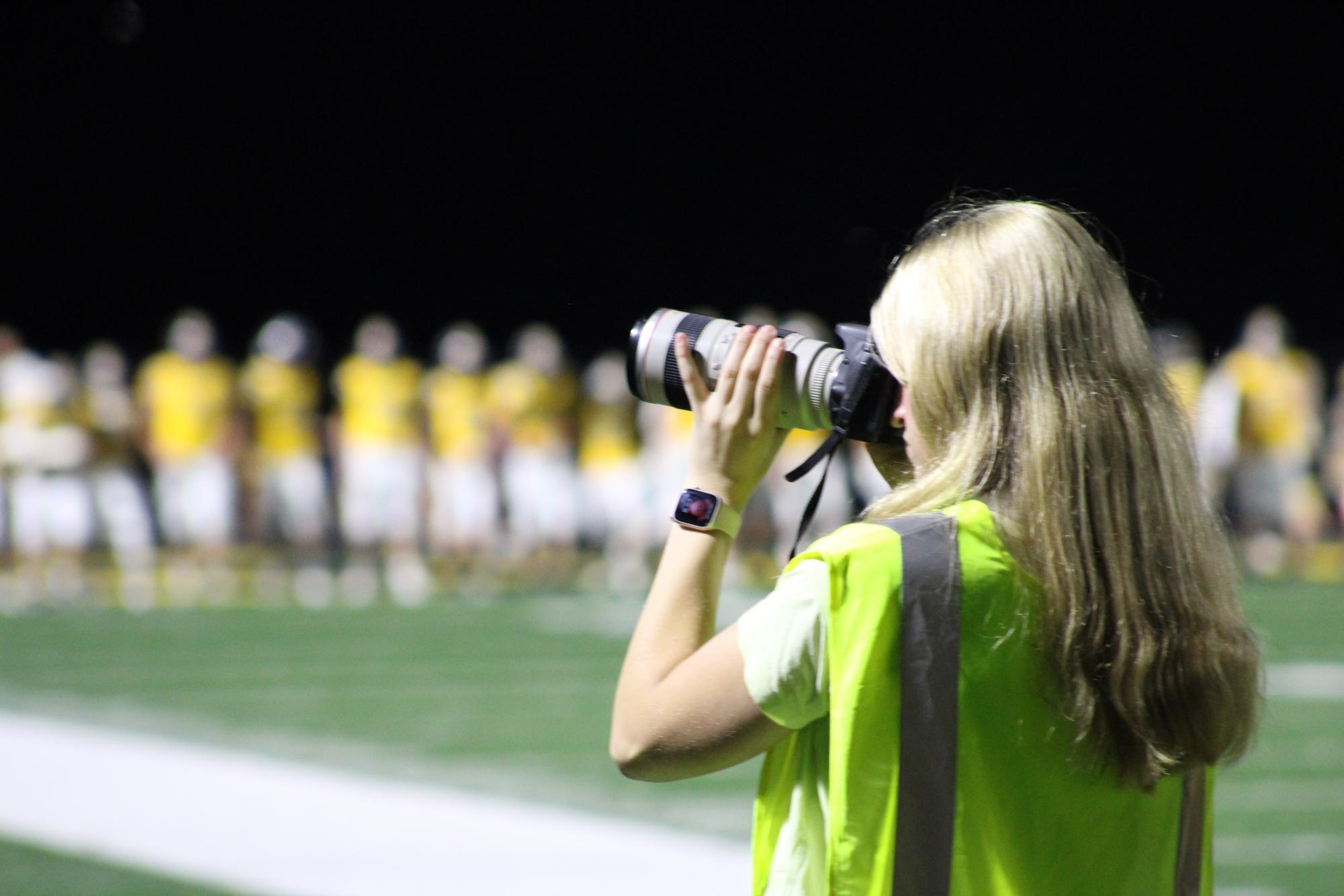 Junior Addie Freund focuses on her photography at an AHS football game. Freund takes photos consistently to share with the journalism department at AHS.