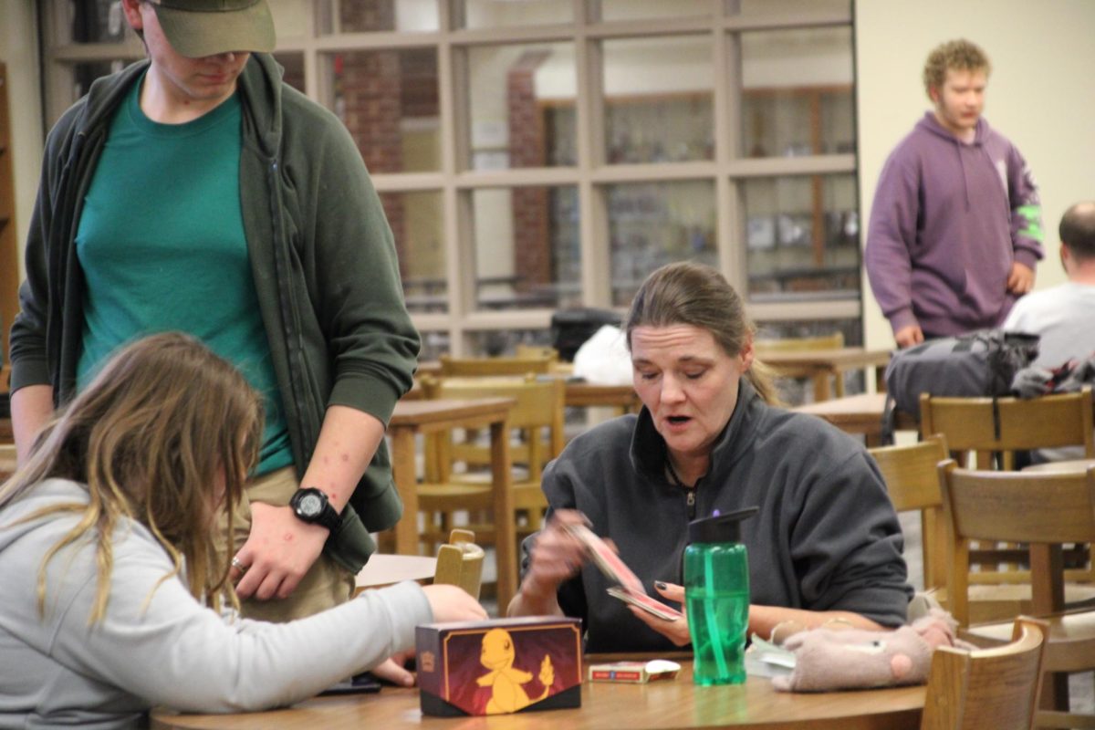 CRIBBAGE! - With his watchful eye, Alex Hayward strolls over to observe as Logan's sister and mother set up a game of Cribbage. Logan's mother had taken it upon herself to teach Logan's sister the rules of Cribbage. You may not see them around AHS, but the pair are considered Game Club regulars.