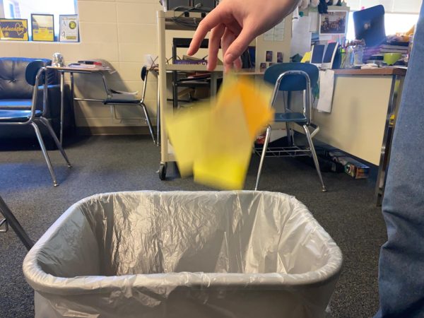 A student drops pieces of paper, a typically recyclable material, into the trash bin.