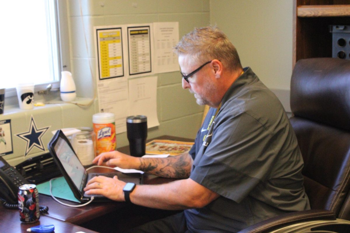 Derek Handel works diligently at his desk. Students surround him, receiving help with their homework. He works with them to get a better understanding of their work. 