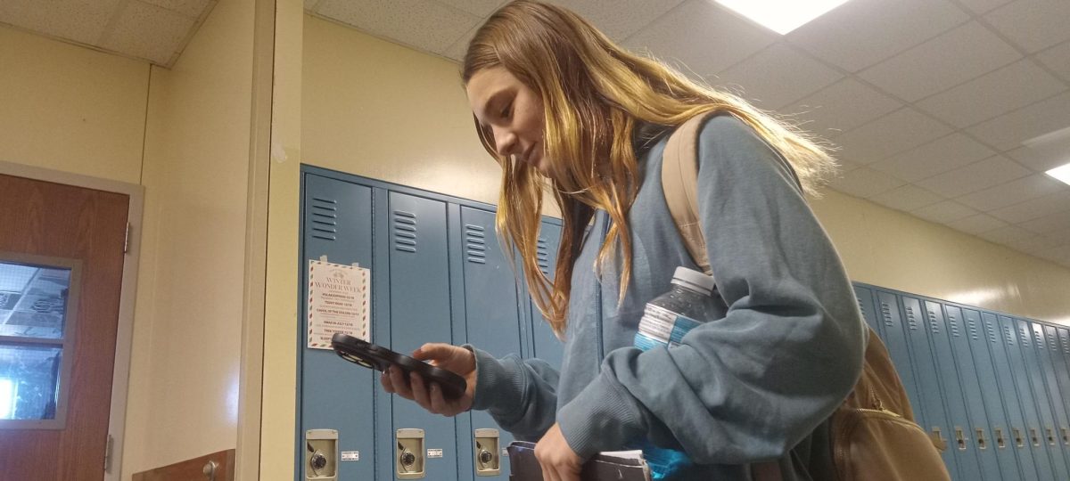 A student walks through social media in the hallway during a passing period on her way to class. 