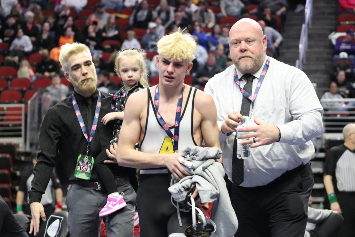 Assistant Coach Dillion Cox, his daughter Octavia Cox, Senior Braxton Hass, and Head Coach Tim Duff walk off the mat after Hass has his hand raised for the last time. 