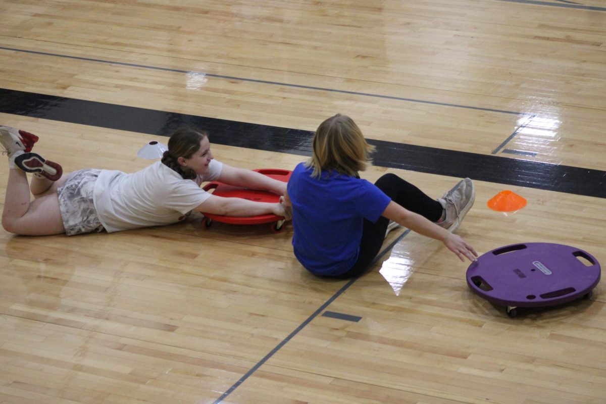 Sophomore Leiah Thomas and enior Natalie Smith fall off the scooters simultaneously. Players try to go as fast as they can while still staying on the scooters.