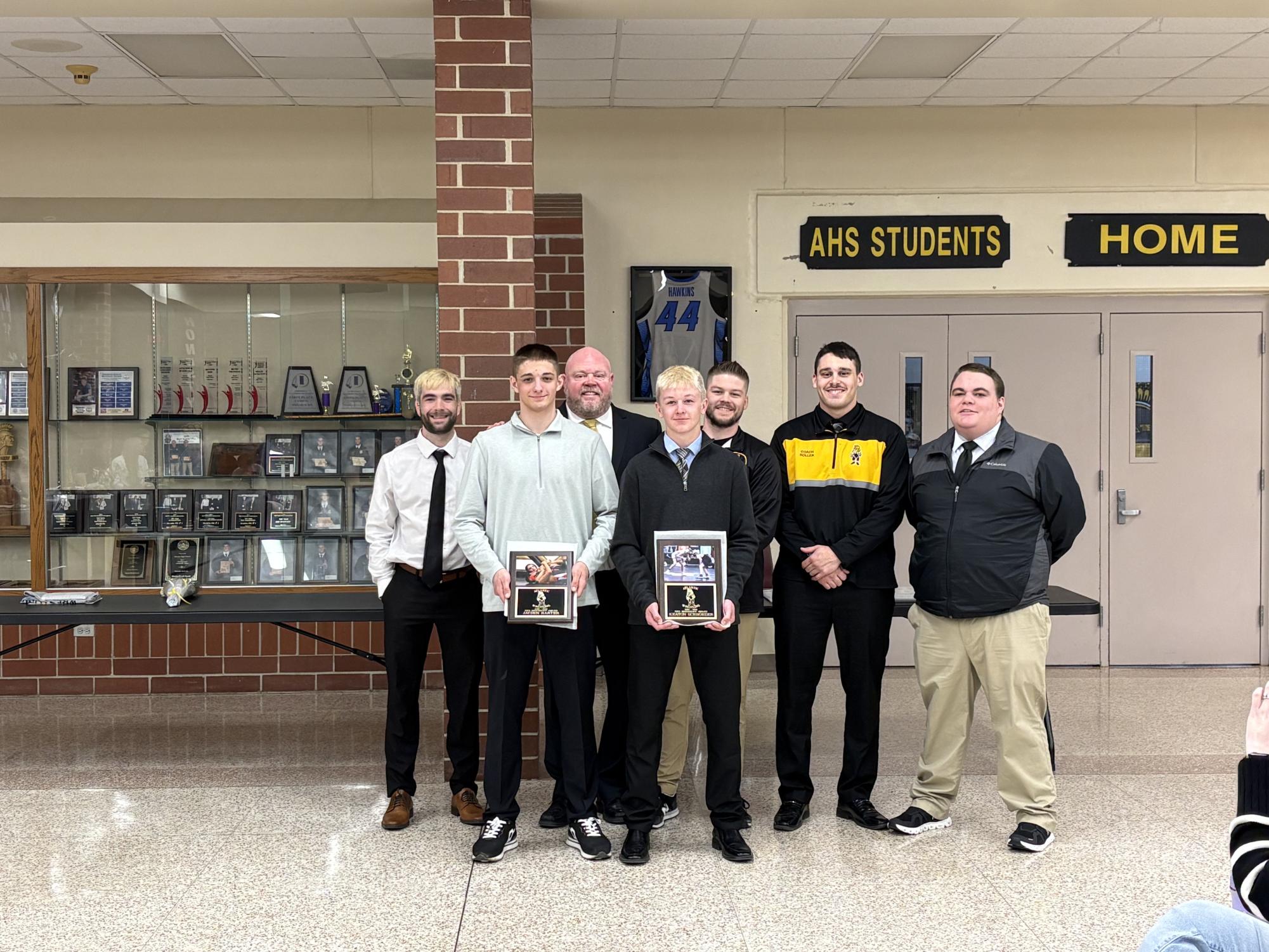 Sophomore Keaton Schroeder and junior Jayden Harter stand in front of the wrestling coaches after being presented with their award.