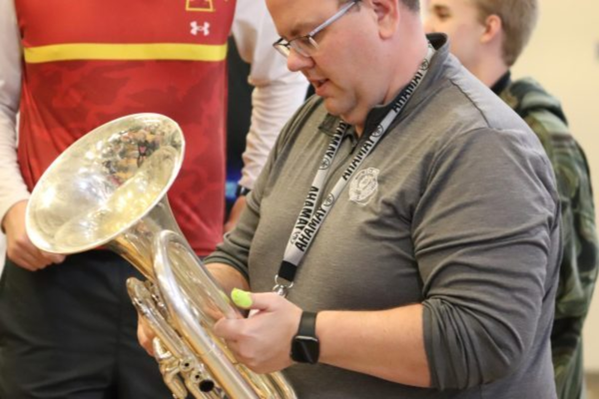 Director Jarrod O'Donnell helps a student with an instrument issue before the performance. Part of his job during pep band was to make sure everything ran smoothly. 