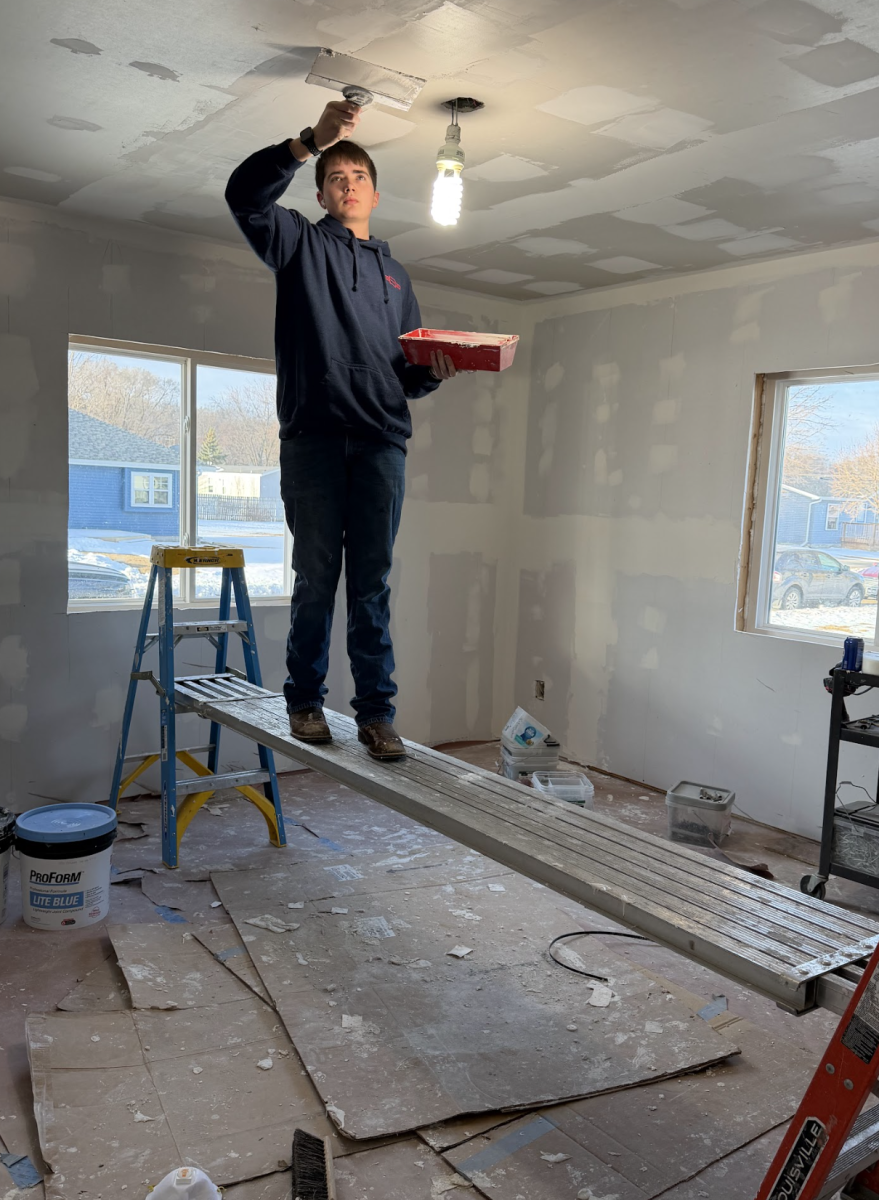 Student Dylen Dreager, Grade 12 patching up the dry wall while standing on a long metal plank. Working on his balance and repairing the dry wall.